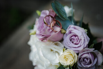 A pair of gold wedding rings on a bride's bouquet with colorful flowers