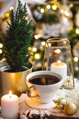 Lifestyle. A cup of tea, a Christmas tree, candles and golden balls on a wooden table against a beautiful bokeh background during the Christmas holidays. Still-life. The concept of home warmth,comfort