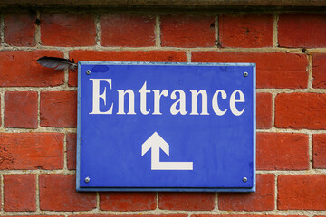 Fototapeta premium Entrance sign with direction arrow. Blue entrance signage on brick wall of building.