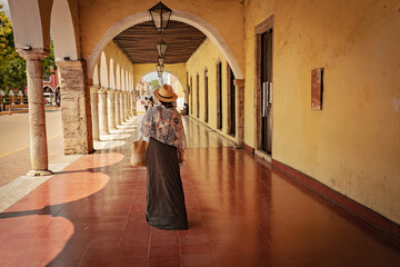 Young woman back view wearing hat walking throung the arch corridor in the historical part of...