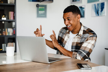 Positive african man gesturing while having video call via laptop at home