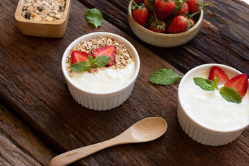 Strawberry yogurt in a wooden bowl with granola, honey, mint and fresh strawberry on wooden background. Health food concept..