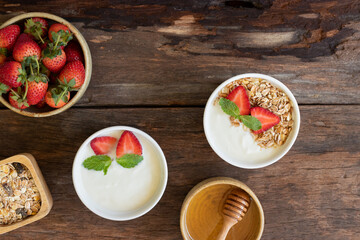 Strawberry yogurt in a wooden bowl with granola, honey, mint and fresh strawberry on wooden background. Health food concept