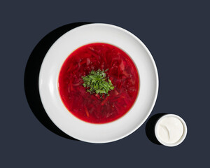 Borscht soup in a white bowl with sour cream top view on blue background isolated