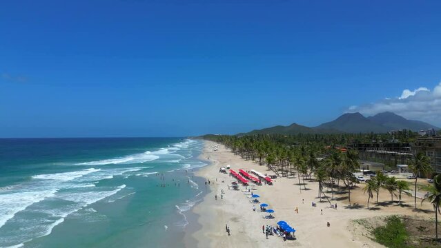 Aerial flight above the sun loungers and parasols on the Playa El Agua tropical beach on the Margarita island, Venezuela. Turquoise water of the Caribbean sea and big waves.