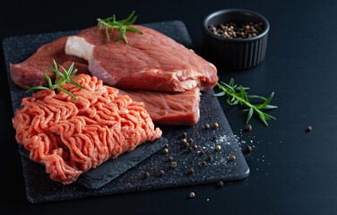 Fresh raw minced meat and cuts of beef, minced meat with herbs and spices on a black table