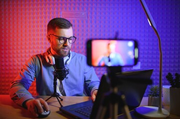 Fototapeta na wymiar vlogger using smartphone to film podcast in studio. blogger with mobile phone, microphone and headphones filming video for social media broadcasting career.