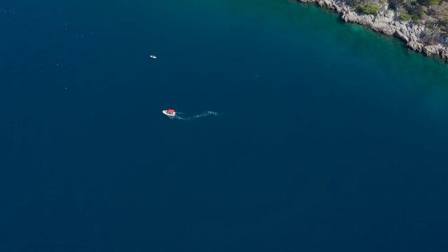 A vertical video from a drone overlooking the depths of the Adriatic Sea, a floating motor boat and a person on the board SUP. Rocky wild coast.