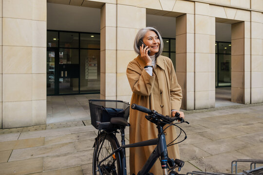 Asian woman using cellphone while standing with bicycle outdoors