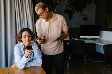 Two multinational colleagues using tablet and smartphone while working in office
