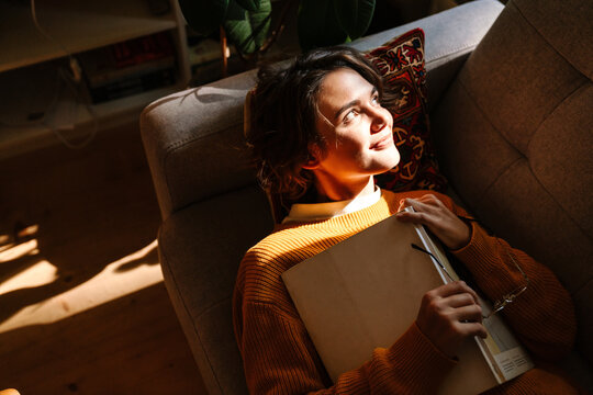 Brunette young woman reading book while resting on couch