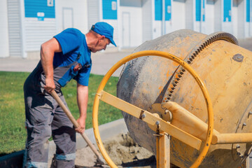 Uniformed construction worker works on construction site on summer day. Elderly bricklayer shovels...