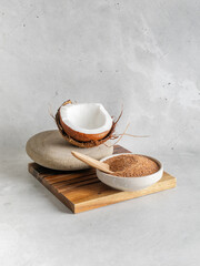Natural bio brown coconut  sugar in a bowl on wooden stand closeup with coconut  on stone background