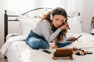 Young girl doing makeup while sitting on bed at home