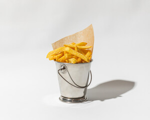 A close-up shot of a bucket filled with delicious French fries, isolated on a white background. The fries are golden brown and crispy, and the bucket has a shiny metallic finish.