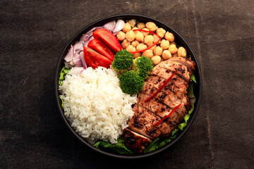 Healthy food grilled chicken has rice and vegetable in bowl on black wood table.