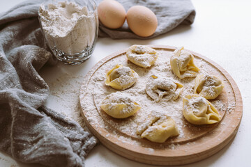 Italian tortellini or dumplings on cutting round wooden board sprinkled with flour. cooking process