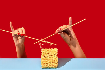 Creative image with female hands knitting instant noodles on blue table over vivid red background....