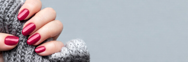 Female hand with knitted scarf and beautiful manicure - viva magenta, burgundy glittered nails with...