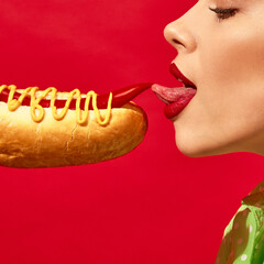 Woman with red lipstick eating spicy hotdog with mustard and chilli over vivid red background....