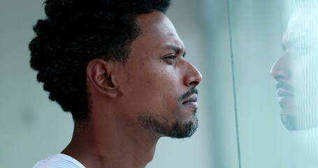 Pensive African man looking out window indoors. Thoughtful black person thinking deeply