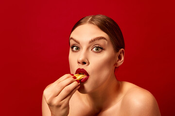 Emotive young woman eating fried potato, fries over vivid red background. Junk food. Food pop art...