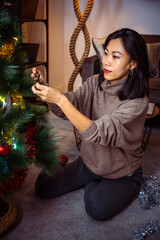 Beautiful Asian girl decorating Christmas tree in her livingroom