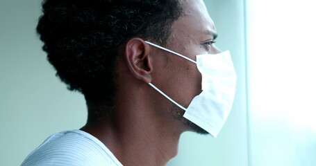 Black man in lockdown staying at home looking out window wearing mask