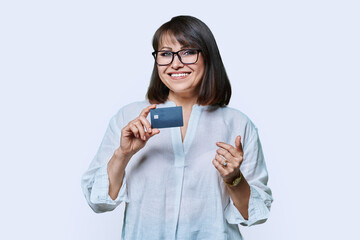 Attractive middle aged smiling woman holding plastic credit card, white background