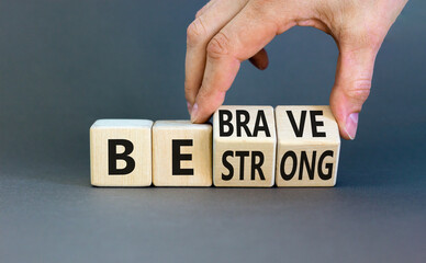 Be strong and brave symbol. Concept word Be strong Be brave on wooden cubes. Beautiful grey table grey background. Businessman hand. Business be strong and brave concept. Copy space.