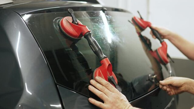 Two white mechanics using professional screen suction cups to take out rear window out of a black car. Indoor shot. High quality 4k footage