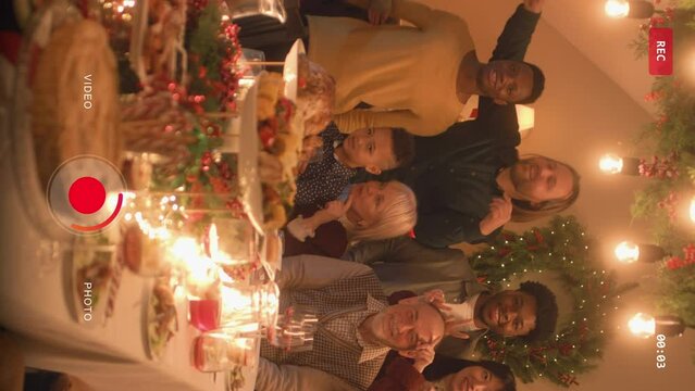Vertical shot of Asian woman sets timer on camera or phone. Happy multi cultural family takes group photo. They celebrating Christmas or New Year. Table with dishes and candles. Camera view.