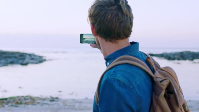 Man, travel and phone at beach to take picture or recording video of view while on vacation with a backpack for freedom and adventure. Male with smartphone at sea to update blog with journey post