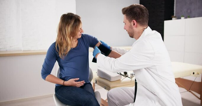 Male Doctor Measuring Blood Pressure Of Pregnant Woman