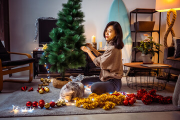 Beautiful Asian girl decorating Christmas tree in her livingroom