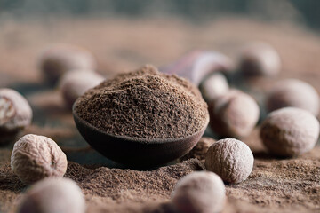 Fototapeta na wymiar Dried ground nutmeg in a wooden spoon with whole nutmeg nearby. Selective focus with extreme blurred foreground and background.