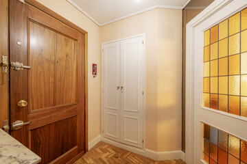 Entrance hall of a house with an armored access door, white wooden doors with leaded glass, oak slatted parquet and a white cabinet with lacquered wood