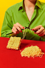 Creative image with woman knitting instant noodles on blue table on vivid red tablecloth over yellow background. Food pop art photography.