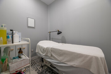 A booth with a stretcher covered with clean towels, an articulated black lamp in a beauty salon