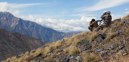 Men in camouflage with weapons are watching high in the mountains.