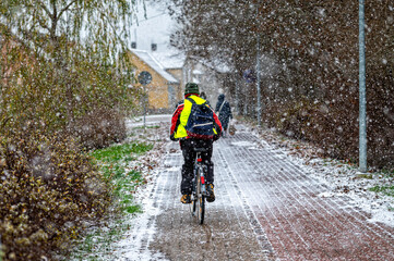 Obraz premium Rear view of a cyclist riding on a paved sidewalk during a snowfall