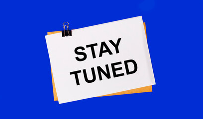 On a bright blue background, an envelope and a sheet of paper with the text STAY TUNED under the paper clip.