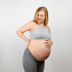 A pregnant girl, on a gray background. Big stomach, back pain.