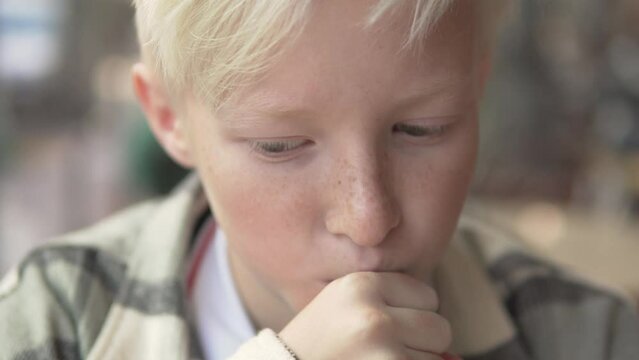 Close-up, a blond boy drinking a drink from a straw.