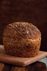 Loaf of whole grain rye bread on a wooden board on a rustic background. Fresh homemade bread with seeds. Copy space.