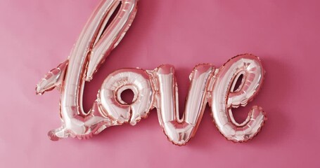 Overhead video of shiny pale pink love text balloon, on pink background with copy space - Powered by Adobe