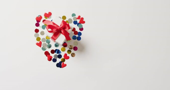 Video of white gift box tied with red ribbon on confetti in heart shape, with copy space