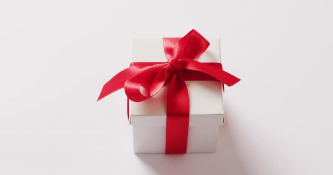 High angle video of white gift box tied with red ribbon, on white background with copy space