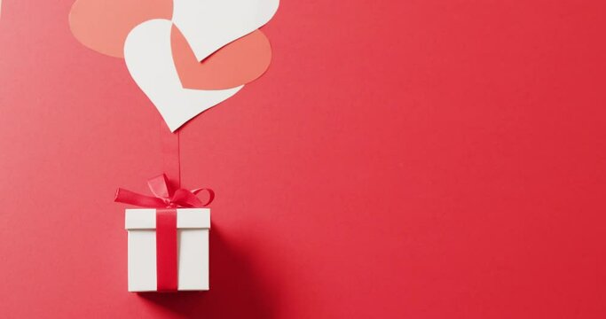 Video of white gift box with red bow and white and red hearts, on red background with copy space