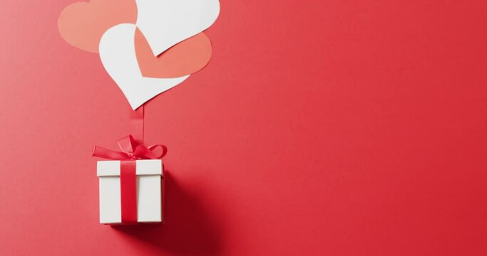 Video of white gift box with red ribbon and red and white hearts, on red background with copy space